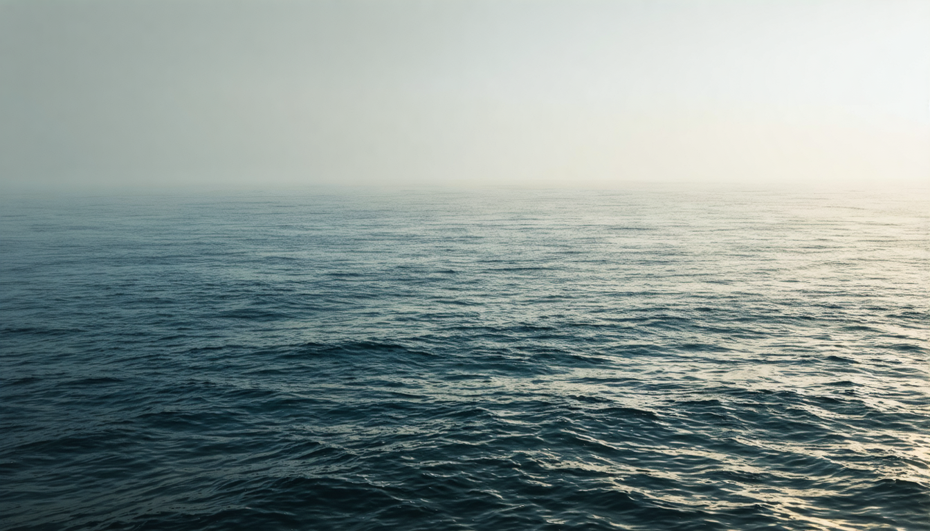 Calm ocean surface at dawn with subtle ripples catching low golden light, horizon line barely distinguishable from overcast sky.