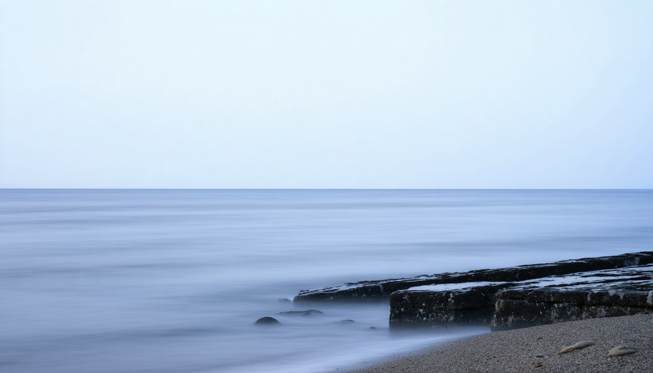 An open sea meeting weathered granite at dawn, soft water eroding stone without any wall to contain it.