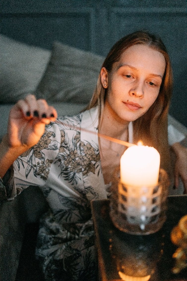 Person lighting a candle with a match in a dim room, candle glow illuminating their face
