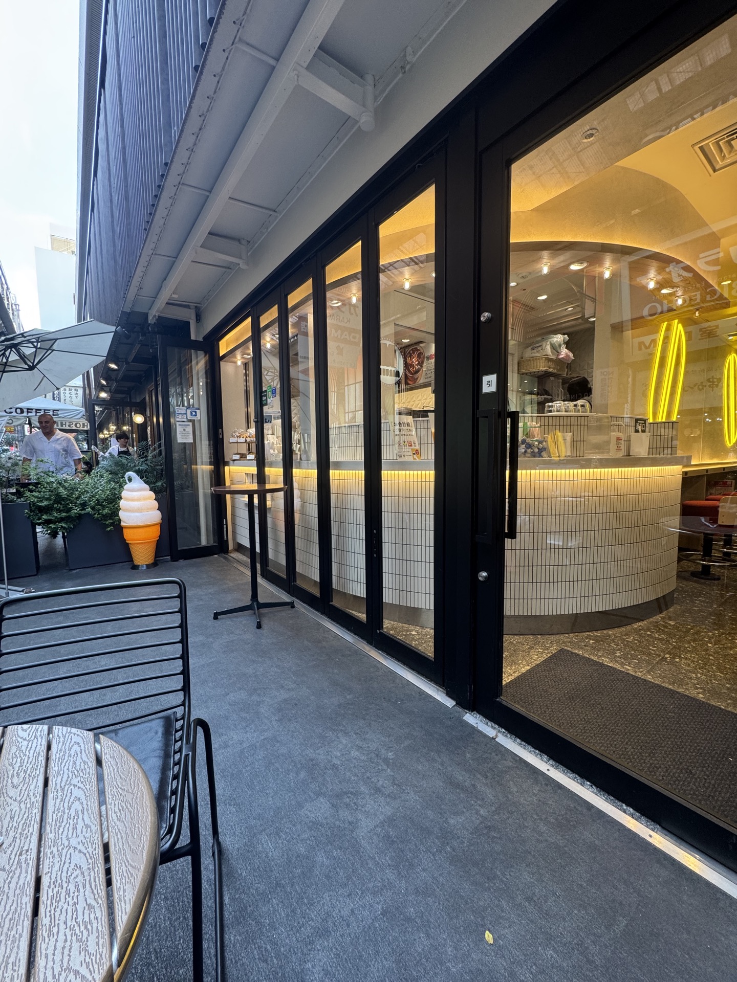 interior of Doutor Stand Namba showing curved white subway tile counter with black grout and yellow neon strip lighting along plaster wall