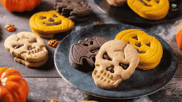 Easy Halloween Cookies Recipe Festive Halloween sugar cookies shaped like skulls, bats, and jack-o'-lanterns displayed on dark plates with small decorative pumpkins.