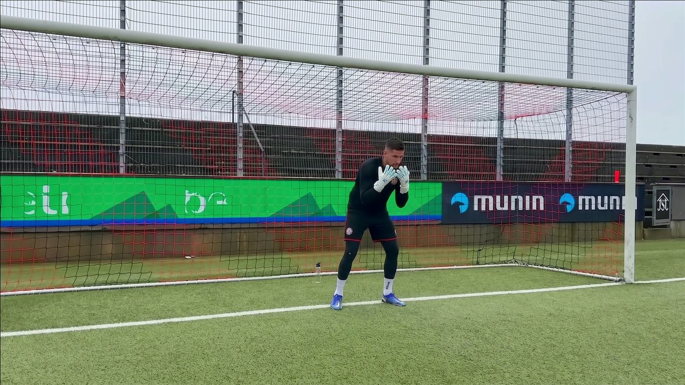 Goalkeeper crouched low in his set position in front of goal, hands out in front, waiting for the ball