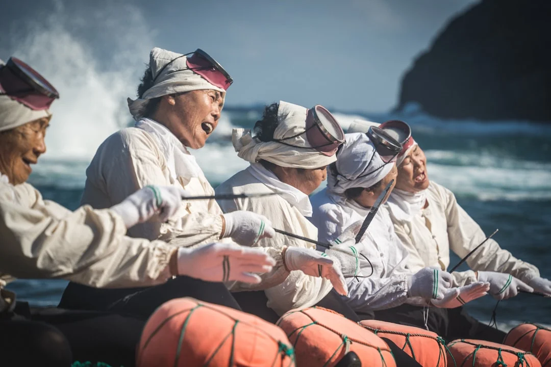 Jeju haenyeo female free divers in traditional white uniforms with diving masks and orange buoys at Umutgae Beach near Seongsan Ilchulbong
