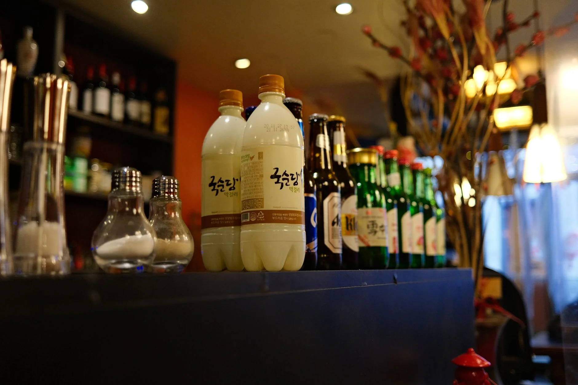 Kooksoondang makgeolli bottles and a row of Korean soju bottles displayed on a bar counter at a Korean restaurant