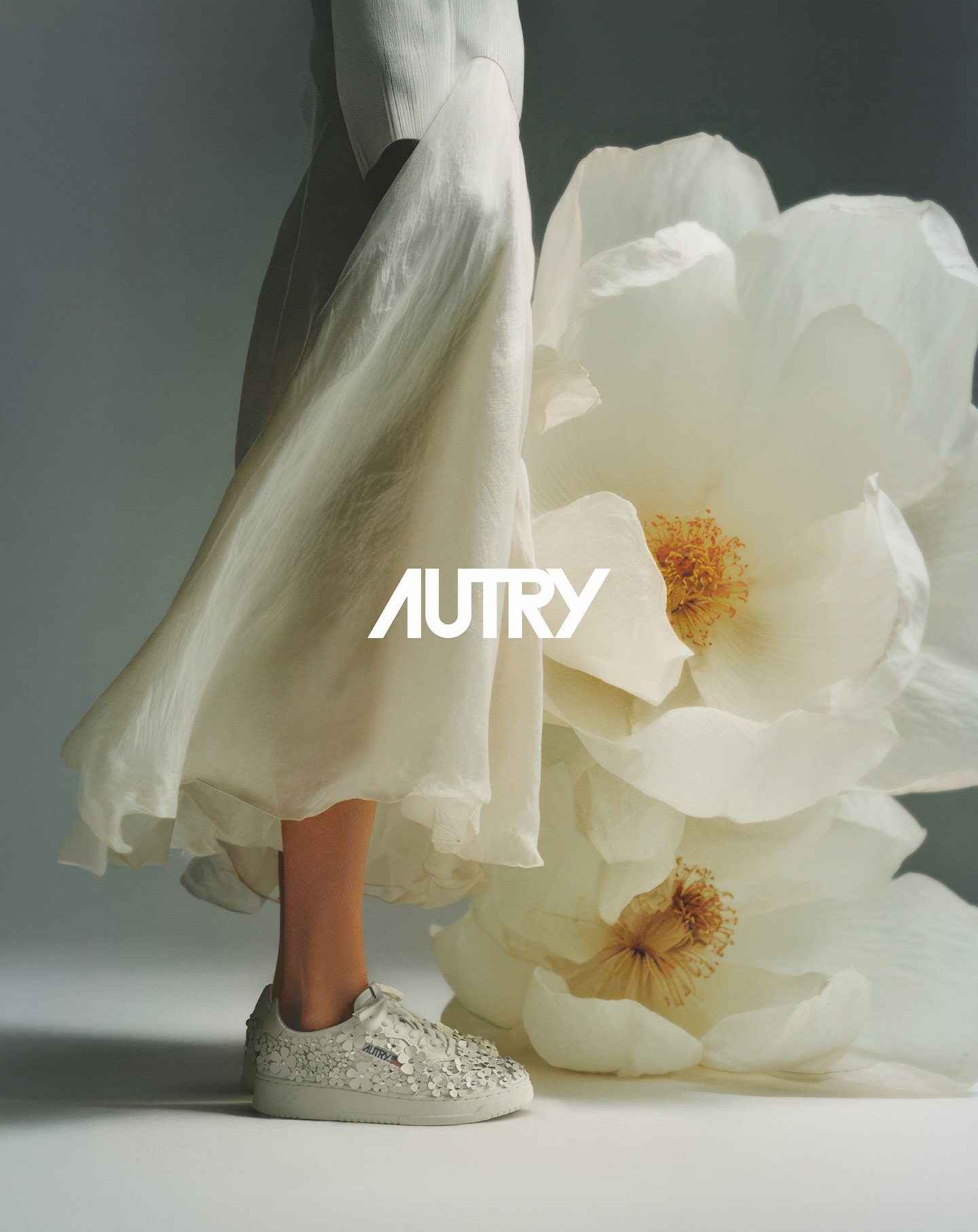 Sneaker bianca Autry Bloom con dettagli floreali indossata accanto a un fiore gigante