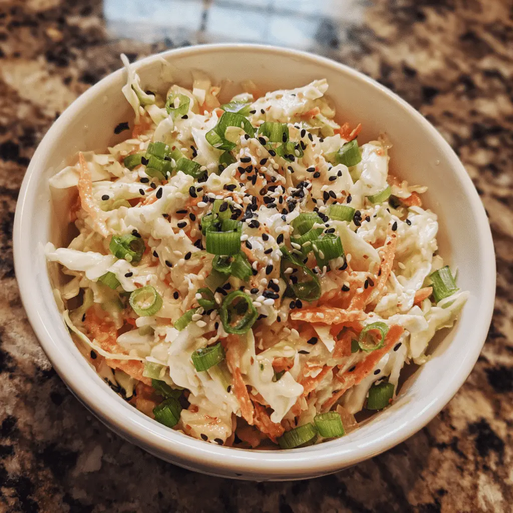 Bowl of colorful Asian sesame slaw with fresh cabbage, carrots, and sesame seeds – a refreshing picnic side dish.