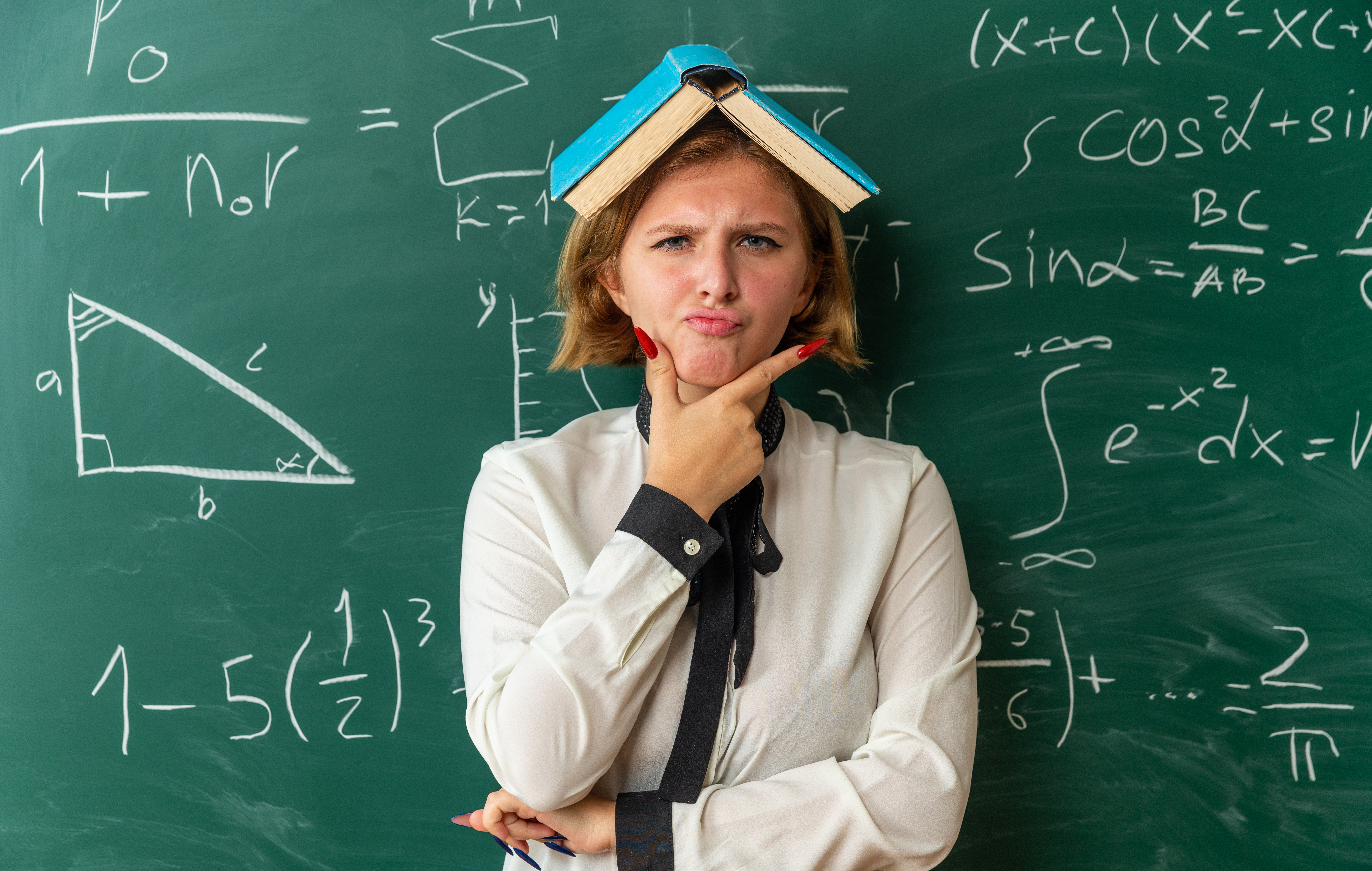 женщина стоит у доски с открытой книгой на голове и задумчивым выражением лица