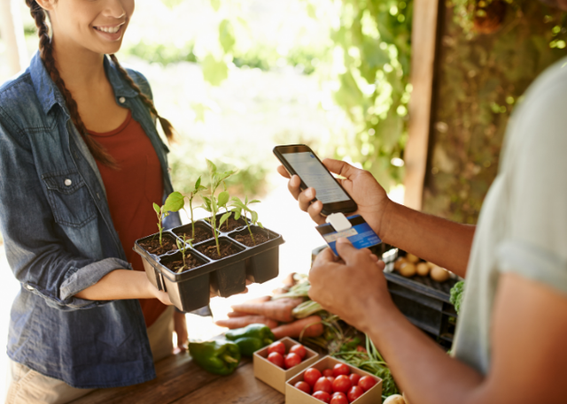 Person using phone to pay at farmers market vendor stand