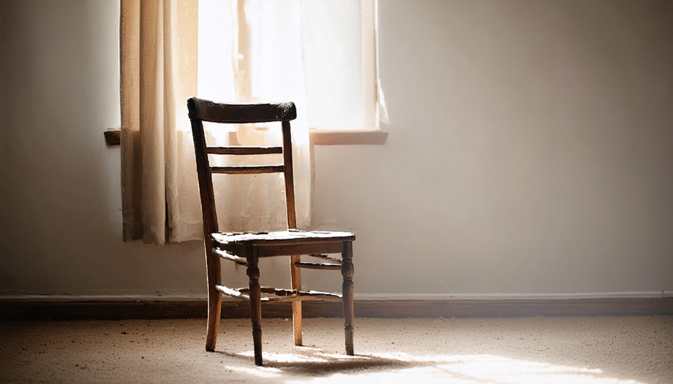 An empty wooden chair in a bare room lit by a single window, with soft dust hanging in the light.
